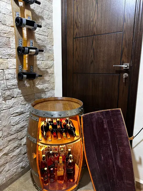 A barrel bar standing open against a stone wall, its interior lit warm, bottles on both shelves.