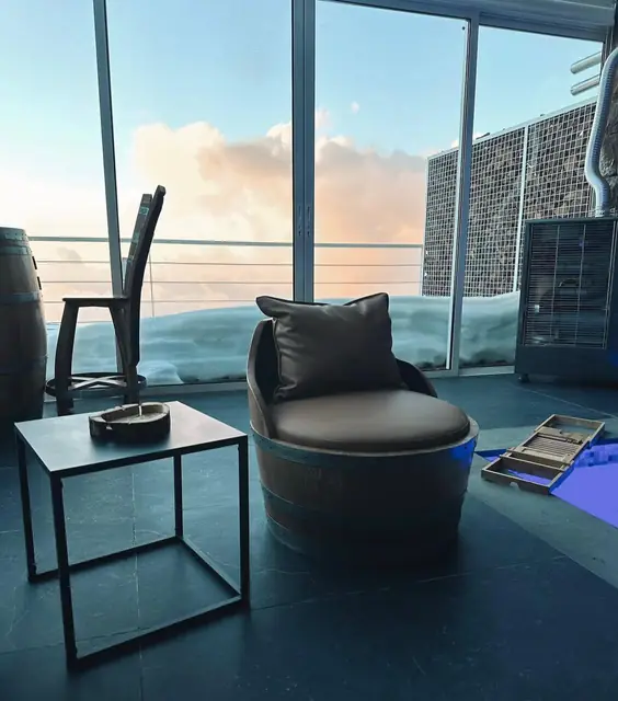 A barrel armchair and a small side table on a rooftop terrace overlooking the sea.