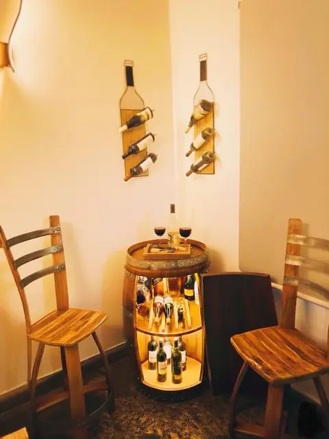 A corner of a room fitted out with two wall racks and an illuminated barrel bar between two chairs.