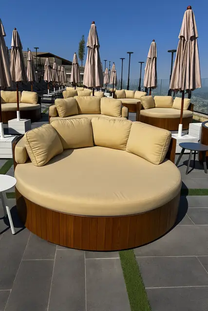A round poolside daybed with a slatted wooden base and pale cushions.