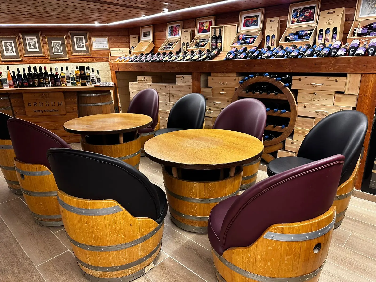 Barrel armchairs upholstered in burgundy and black, grouped around round oak tables in a winery lounge.