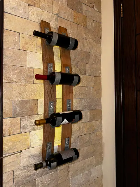 A backlit oak wall rack holding four bottles, mounted on a stone wall.